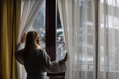 Beyaz bornozlu bir kadın kışın Avusturya 'da bir SPA' nın balkonunda dikiliyor. Onun ıslak saçı var. Önündeki dağların manzarasının tadını çıkarıyor. Rahatlamış hissediyor.