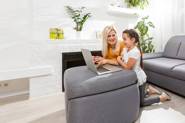 Usmívající se mladá matka a dcera studující online třídy v domácí kanceláři v moderním obývacím pokoji — Stock fotografie