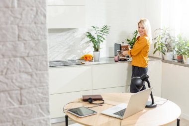 Genç bir kadın mutfakta oturuyor ve dizüstü bilgisayarla çalışıyor..