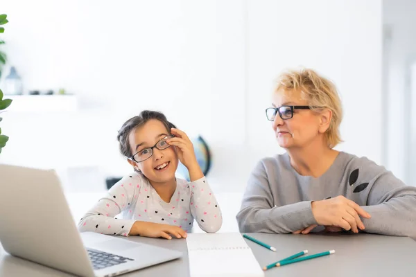 La nonna matura aiuta il bambino con i compiti a casa. Soddisfatto vecchia nonna aiutare la nipote a studiare in soggiorno. Ragazzina che scrive sul taccuino con l'insegnante anziana seduta accanto a lei — Foto Stock