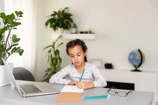 Klein meisje doet haar huiswerk thuis en met behulp van een laptop — Stockfoto