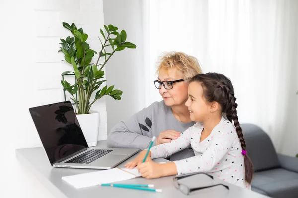 Užitečná babička. Pomohla milující babička pomáhá její roztomilé vnučky dělat domácí úkoly — Stock fotografie