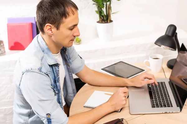 Heureux jeune homme souriant, car il travaille sur son ordinateur portable pour faire toutes ses affaires tôt le matin avec sa tasse de café — Photo