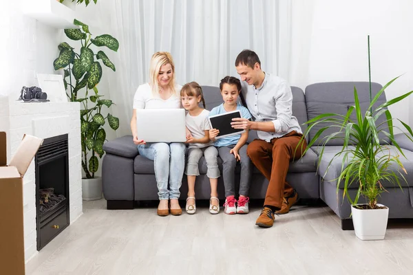 Ung glad avslappnad familj med två barn och par sitter på soffan och tittar på rolig video eller karikatyrer i touchpad — Stockfoto