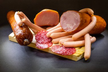 Farklı bir jambon ve salamlı, koyu bir arka planda otlar.