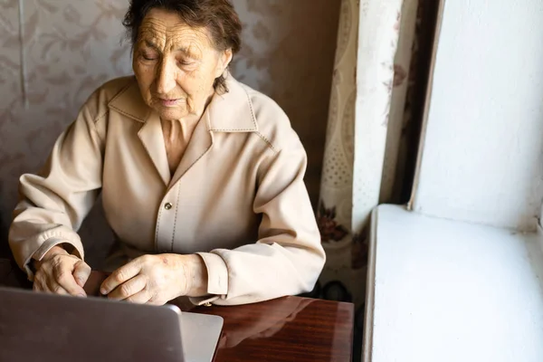 stock image Senior woman use laptop. She looks very surprised. Surfing in a browser and social media. Laptop on the table. Using technology in old age concept