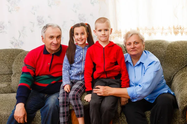 Joyeux jeune garçon et jeune fille avec leurs grands-parents riants souriant à la caméra alors qu'ils posent ensemble à l'intérieur — Photo