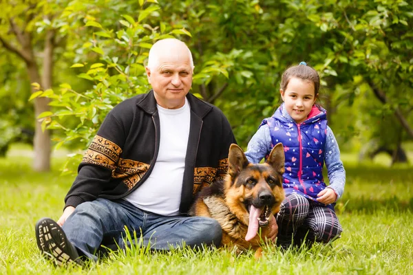 Grootvader met kleindochter en een hond in de tuin — Stockfoto