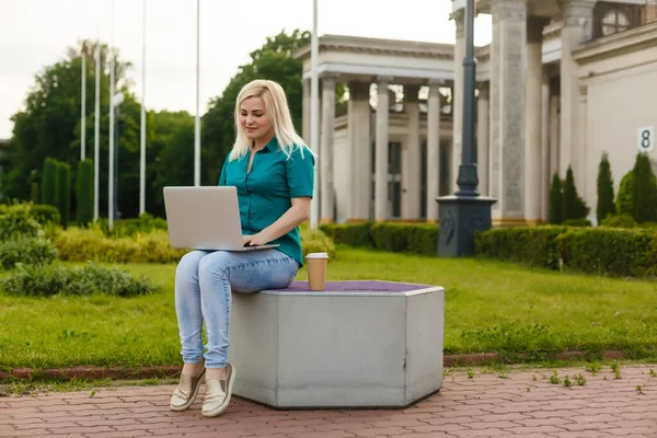 Bela jovem loira com um laptop no parque em um dia quente de verão — Fotografia de Stock