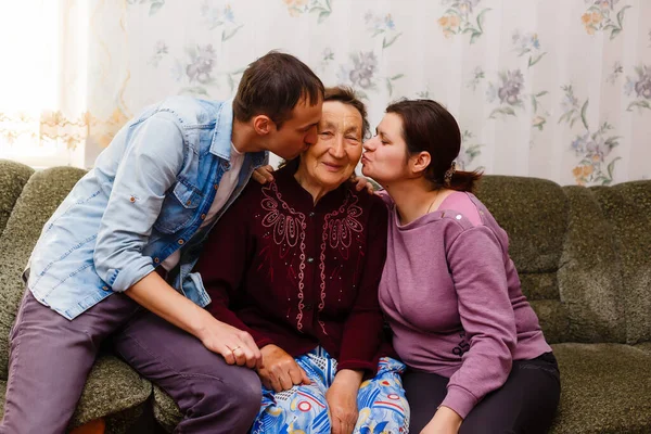 Volwassen lachende kleinkinderen omhelzen oudere grootmoeder blij haar te zien missen, bezoek van liefdevolle familieleden genieten van communicatie, knuffelen als symbool van verbondenheid, liefde en steun concept — Stockfoto