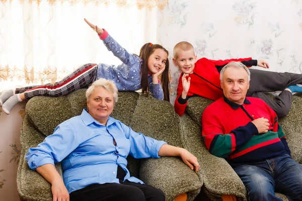 Jovem e menina feliz com seus avós rindo sorrindo para a câmera enquanto posam juntos dentro de casa — Fotografia de Stock