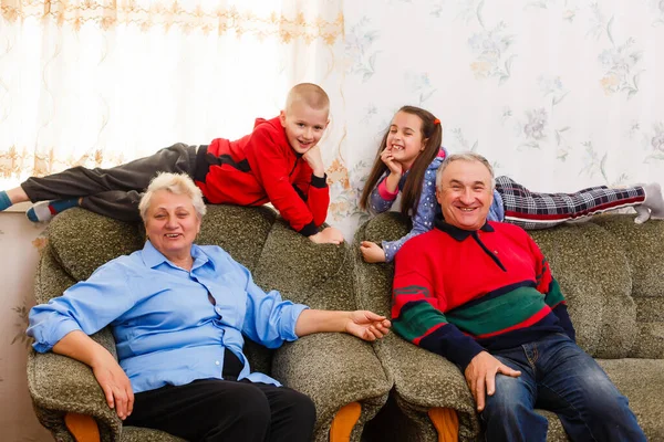 Kleinkinderen springen op de bank met hun grootouders in de woonkamer — Stockfoto