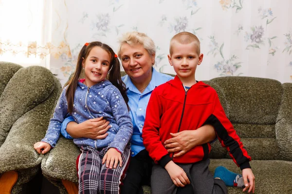 Volwassen lachende kleinkinderen omhelzen oudere grootmoeder blij haar te zien missen, bezoek van liefdevolle familieleden genieten van communicatie, knuffelen als symbool van verbondenheid, liefde en steun concept — Stockfoto