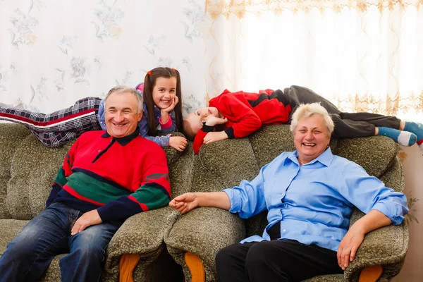 Jovem e menina feliz com seus avós rindo sorrindo para a câmera enquanto posam juntos dentro de casa — Fotografia de Stock