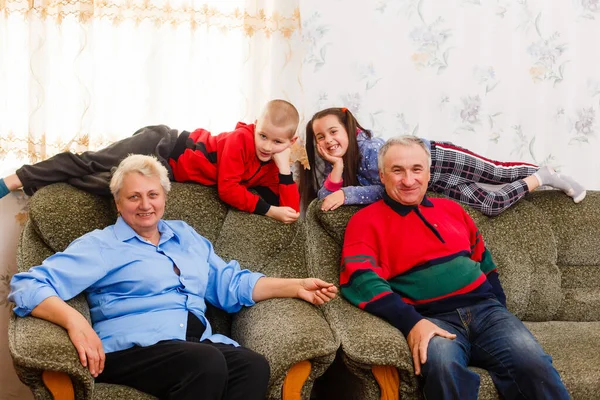 Jovem e menina feliz com seus avós rindo sorrindo para a câmera enquanto posam juntos dentro de casa — Fotografia de Stock