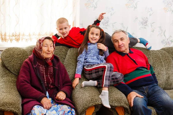 Mutlu genç bir oğlan ve kız kameraya gülümseyen büyükanneleri ve büyükbabaları içeride poz verirken — Stok fotoğraf