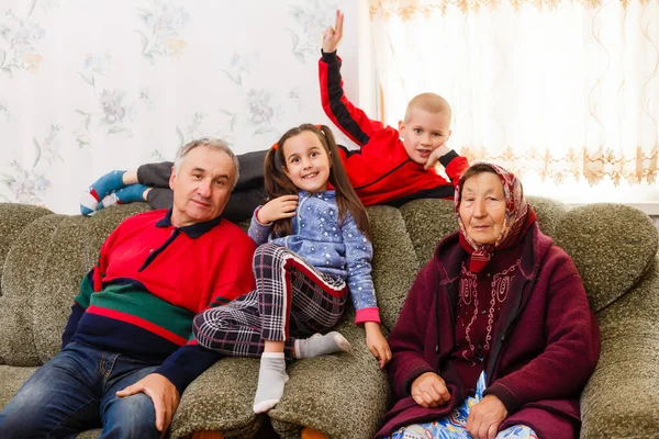 Kleinkinderen springen op de bank met hun grootouders in de woonkamer — Stockfoto