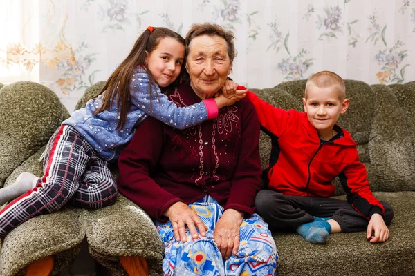 Closeup portrait of happy great-grandmother with great-grandchildren on the sofa at home — Stock Photo, Image