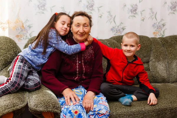 Volwassen lachende kleinkinderen omhelzen oudere grootmoeder blij haar te zien missen, bezoek van liefdevolle familieleden genieten van communicatie, knuffelen als symbool van verbondenheid, liefde en steun concept — Stockfoto