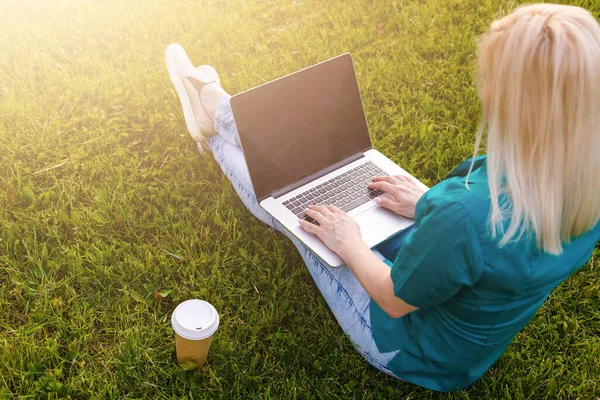 Hermosa joven rubia con un ordenador portátil en el parque en un cálido día de verano — Foto de Stock
