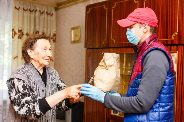Una anciana se queda en casa. Entrega de comida en una máscara médica a los ancianos. —  Fotos de Stock