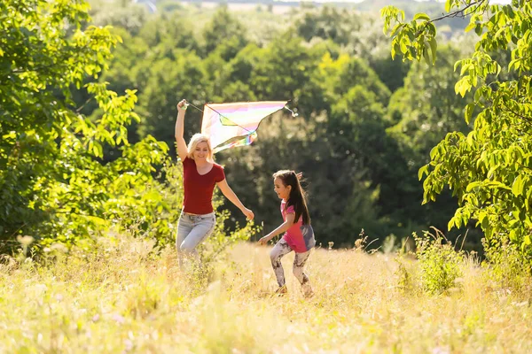 Glückliche Familie Mutter und Kind laufen im Sommer mit dem Drachen auf der Wiese in der Natur — Stockfoto