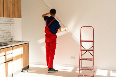 Gereken alçıpan genişliğini ölçmek ve etiket işareti koymak için kural kullanan tanınamayan tamirci ustasının görünüm fotoğrafının gerisine geç