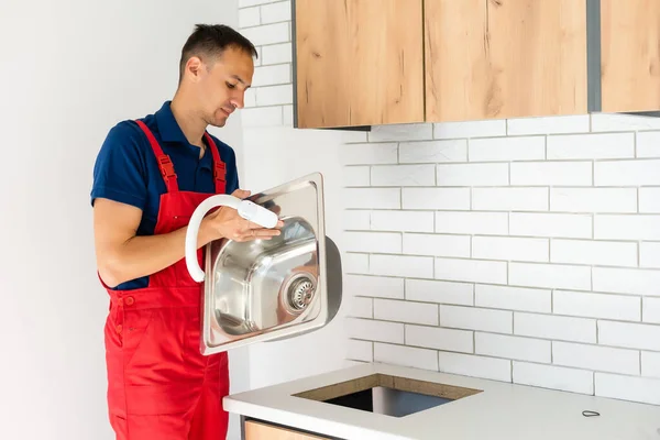 Lächelnder erwachsener Reparateur mit Rohr und Schraubenschlüssel bei der Reparatur des Wasserhahns in der Küche — Stockfoto