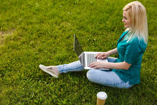 俯瞰坐在公园绿草上，手握键盘，手握笔记本电脑的女人的照片。电脑屏幕模拟。学生在户外学习。文本的复制空间 — 图库照片