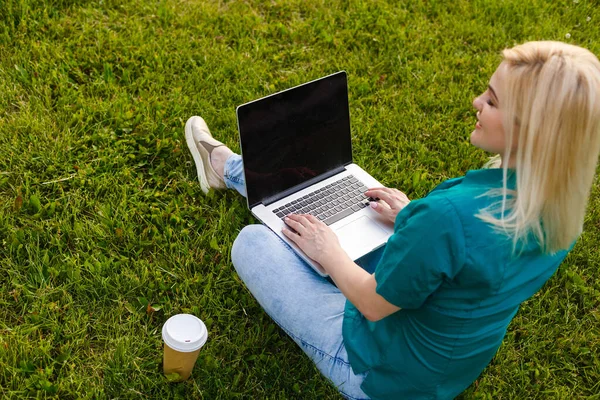 俯瞰坐在公园绿草上，手握键盘，手握笔记本电脑的女人的照片。电脑屏幕模拟。学生在户外学习。文本的复制空间 — 图库照片