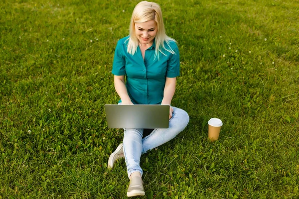 Bela jovem loira com um laptop no parque em um dia quente de verão — Fotografia de Stock