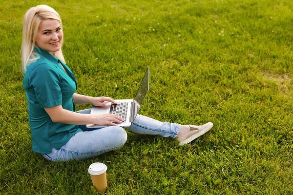 Hermosa joven rubia con un ordenador portátil en el parque en un cálido día de verano — Foto de Stock