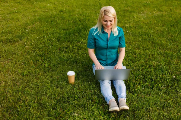 Vista superior de la mujer sentada en el parque en la hierba verde con el ordenador portátil, las manos en el teclado. Una maqueta de la pantalla del ordenador. Estudiante estudiando al aire libre. Copiar espacio para texto — Foto de Stock