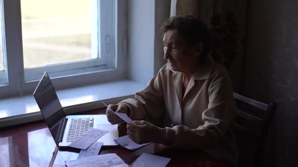Een zeer oude vrouw zit aan een tafel en controleert rekeningen voor een appartement — Stockvideo