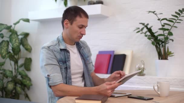 Man die thuis met tablet aan tafel werkt — Stockvideo