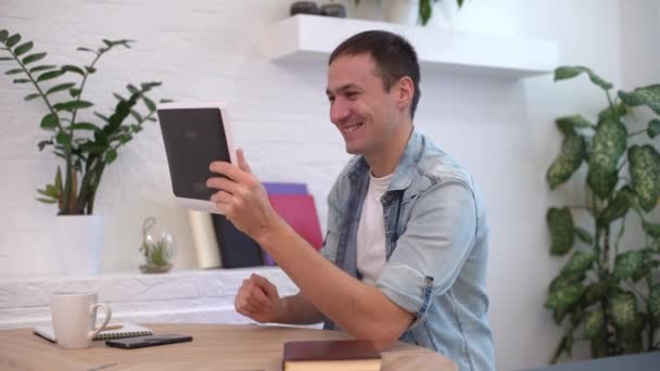 Man heeft een online gesprek met zijn collega, vriend, zitten op de bank thuis, met behulp van gadget, tablet computer, bezig blijven in het weekend, slow motion. — Stockvideo