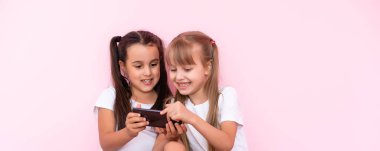 Pembe arka planda akıllı telefonu olan iki küçük kız.