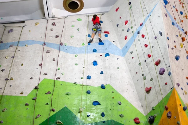 Sportief meisje klimmen kunstmatige rots op praktische muur in de sportschool — Stockfoto