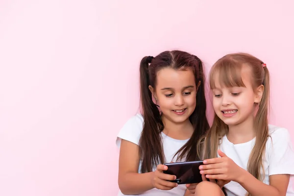 Dos niñas con un teléfono inteligente sobre un fondo rosa —  Fotos de Stock