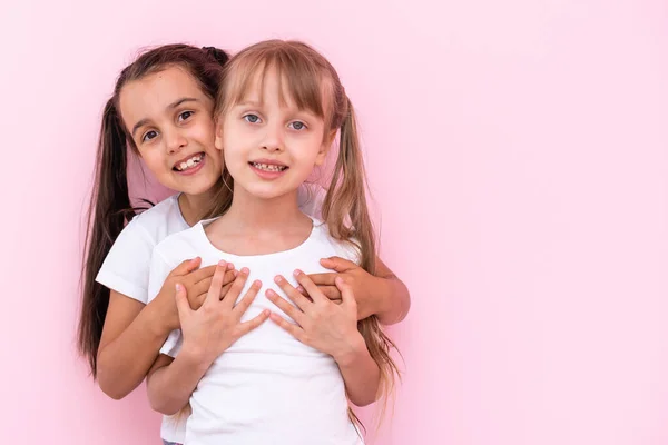 Twee kleine meisjes die elkaar knuffelen. Geïsoleerd op een roze achtergrond — Stockfoto