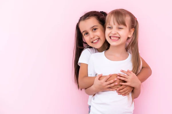 Duas meninas a abraçarem-se. Isolado em um fundo rosa — Fotografia de Stock
