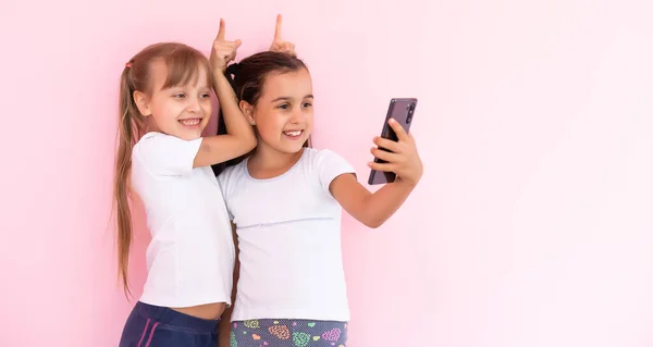 Dwie małe dziewczynki ze smartfonem na różowym tle — Zdjęcie stockowe
