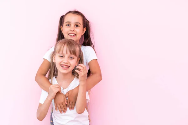 Twee kleine meisjes die elkaar knuffelen. Geïsoleerd op een roze achtergrond — Stockfoto