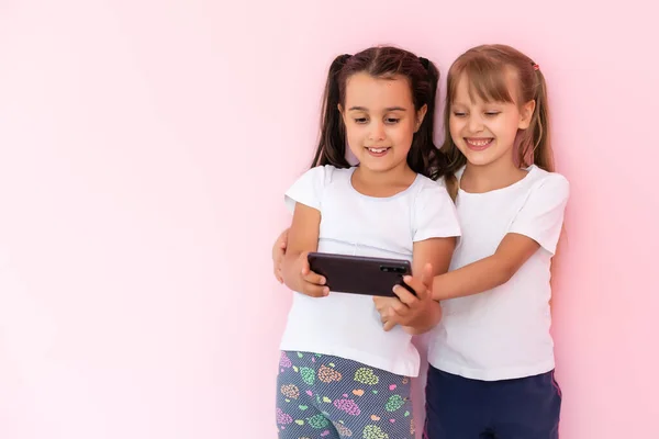 Dwie małe dziewczynki bawiące się smartfonami na różowym tle — Zdjęcie stockowe