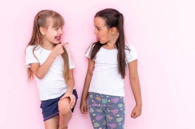 Sırt sırta verip pembe arka planda izole bir şekilde sırta saça örülmüş iki öfkeli genç kız resmi.