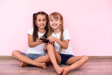 Pembe arka planda akıllı telefonlarla oynayan iki küçük kız.