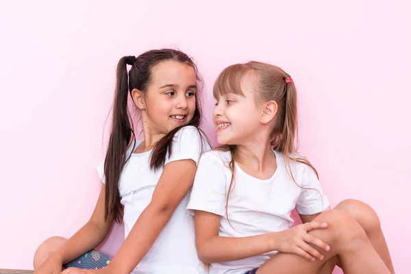 Två små flickor som sitter på golvet och tittar upp. Isolerad på en rosa bakgrund — Stockfoto