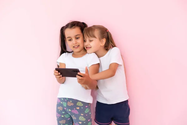 Mensen, kinderen, technologie, vrienden en vriendschapsconcept - gelukkige kleine meisjes met smartphones op de vloer in het thuisonderwijs, school gebruiken een smartphone en glimlachen — Stockfoto