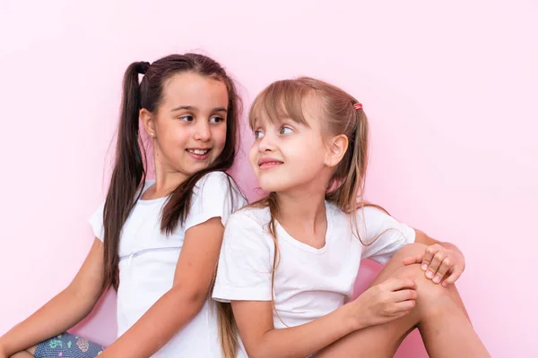 Twee kleine meid die op de vloer zit en omhoog kijkt. Geïsoleerd op een roze achtergrond — Stockfoto