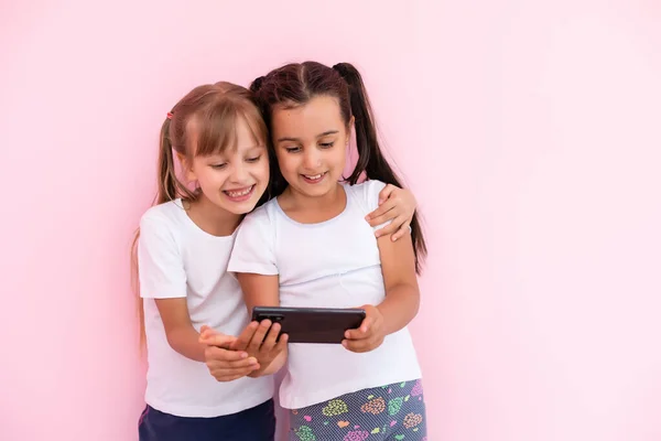 Zwei kleine Mädchen spielen mit Smartphones auf rosa Hintergrund — Stockfoto